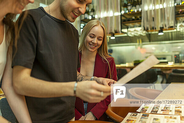 Smiling male and female friends reading menu at bar