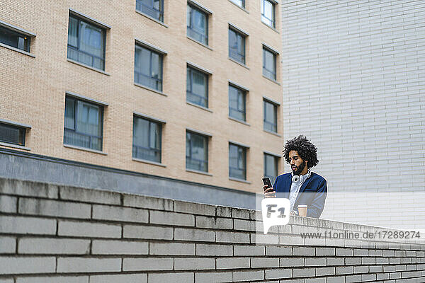 Männlicher Unternehmer  der ein Mobiltelefon benutzt  während er sich auf eine Stützmauer stützt