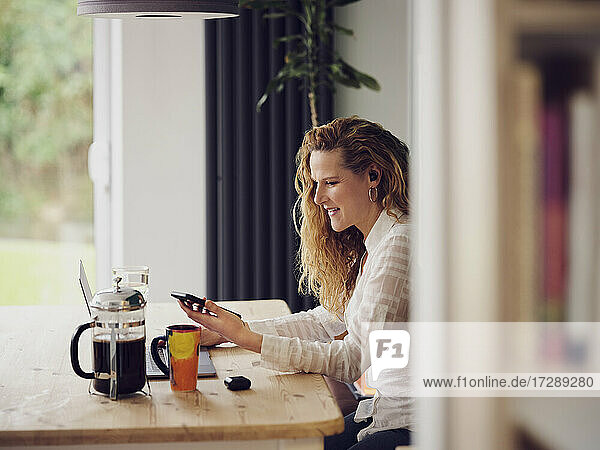 Smiling businesswoman using mobile phone while working at home