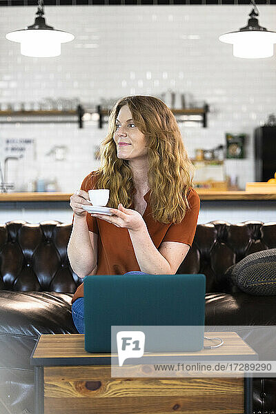 Businesswoman having coffee while sitting in front of laptop at office cafeteria