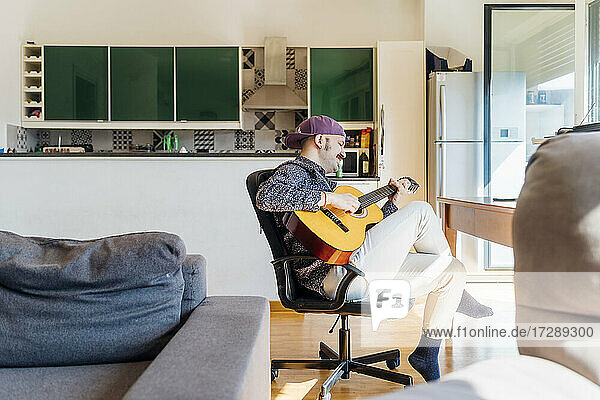 Mann spielt Gitarre auf einem Stuhl zu Hause