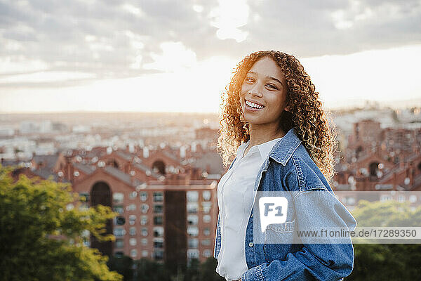 Lächelnde Frau in Jeansjacke in der Stadt bei Sonnenuntergang