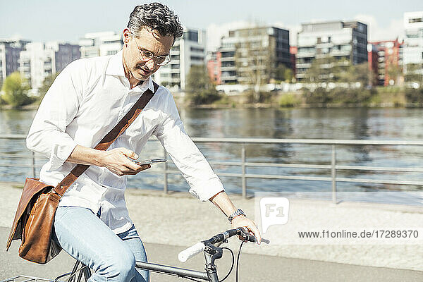 Businessman using mobile phone while cycling bicycle on sunny day