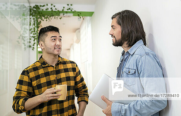 Männliche Mitarbeiter diskutieren im Stehen im Büro miteinander