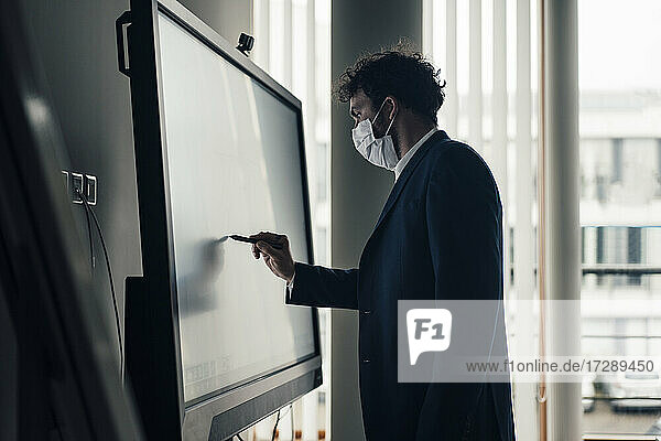 Male entrepreneur with face mask writing on projection screen in office