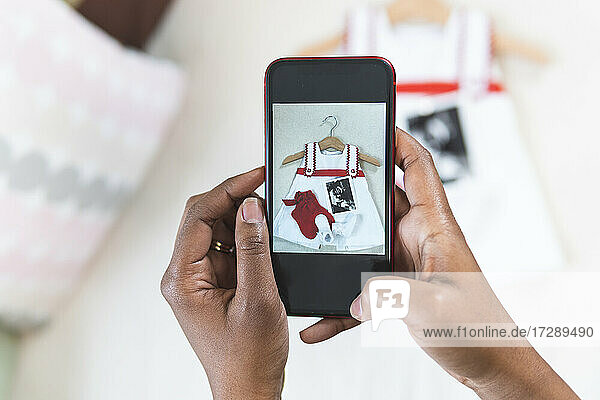 Woman photographing baby clothing through smart phone