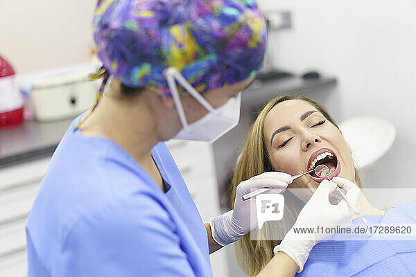 Female dentist wearing surgical gloves examining patient's teeth at medical clinic