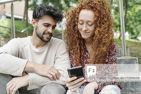 Lächelndes junges Paar benutzt Smartphone auf Stufen im Park