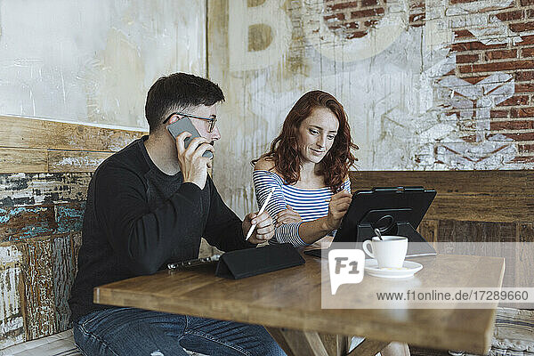 Männlicher Berufstätiger  der mit seinem Smartphone spricht  während er mit einer Kollegin in einem Café sitzt