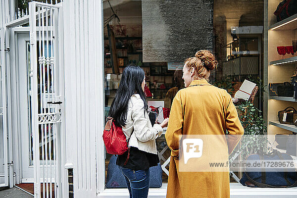 Frau mit Rucksack im Gespräch mit einer Freundin vor einem Kaffeehaus