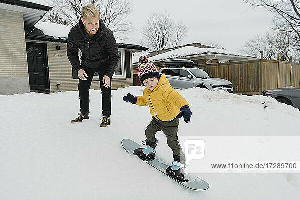 Man looking at son learning snowboarding outside house