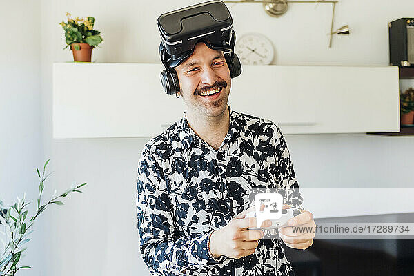 Happy man with virtual reality headset holding game controller at home