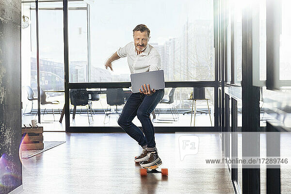 Mature businessman skateboarding looking at laptop in office