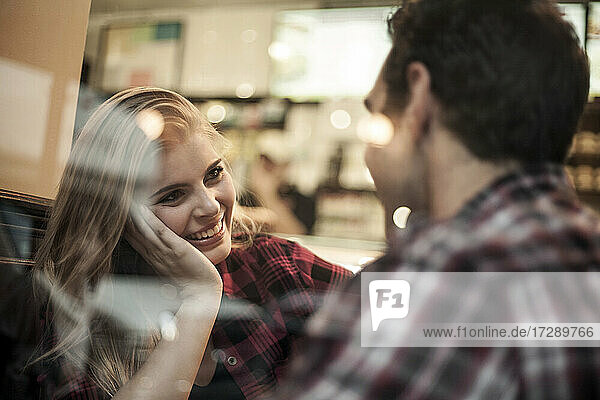 Lächelnde Frau sieht ihren Freund durch das Fenster eines Cafés an