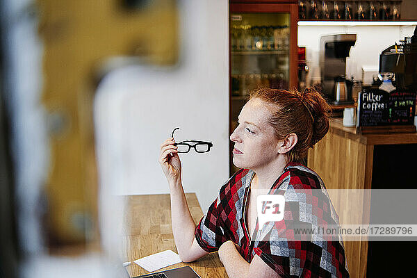 Frau mit Brille  die im Café sitzt und nachdenkt