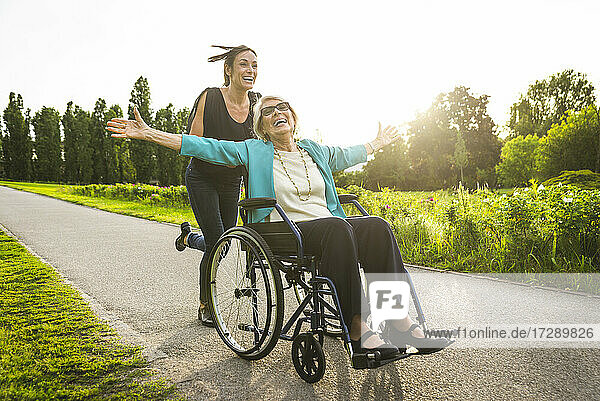 Glückliche Enkelin  die ihre im Rollstuhl sitzende Großmutter im Park schiebt