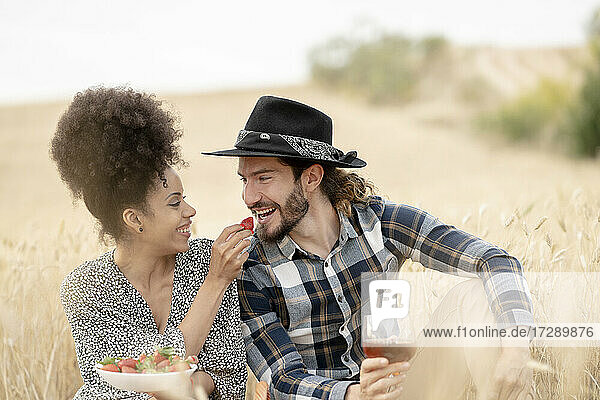 Frau füttert einen Mann mit Erdbeeren  während sie beim Picknick auf einer Wiese sitzt