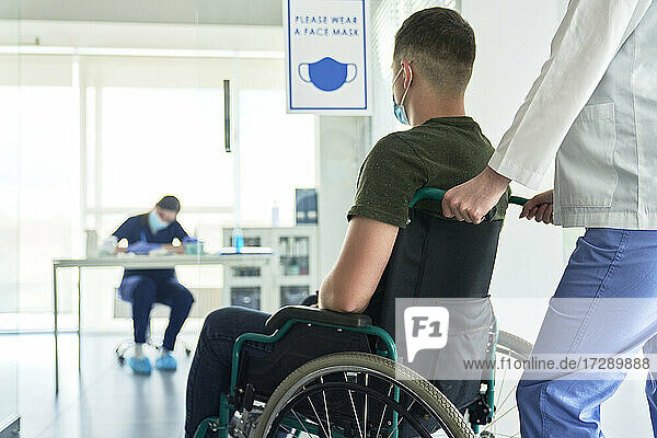 Eine Mitarbeiterin des Gesundheitswesens bringt einen Patienten im Rollstuhl zum COVID-19-Impfzentrum