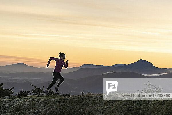 Weibliche Läuferin läuft auf einem Hügel vor dramatischem Himmel
