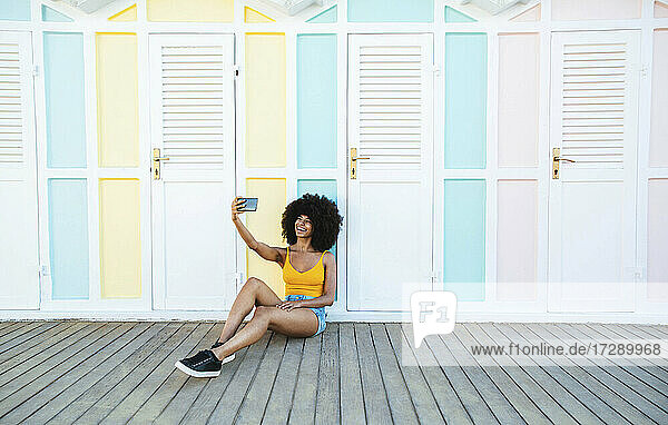 Smiling woman taking selfie in front of beach hut