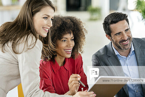 Smiling male and female professionals with graphics tablet looking away in office