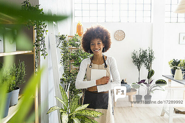 Weibliche Ladenbesitzerin mit digitalem Tablet  die lächelnd in einem Pflanzengeschäft steht
