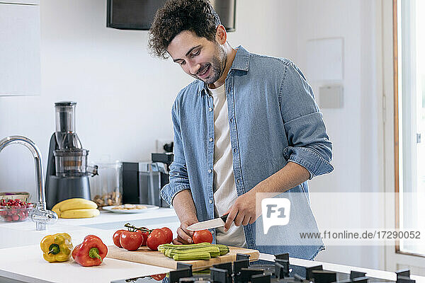 Lächelnder erwachsener Mann  der in der Küche zu Hause Tomaten schneidet