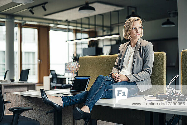 Unternehmerin schaut weg  während sie auf dem Schreibtisch im Büro sitzt