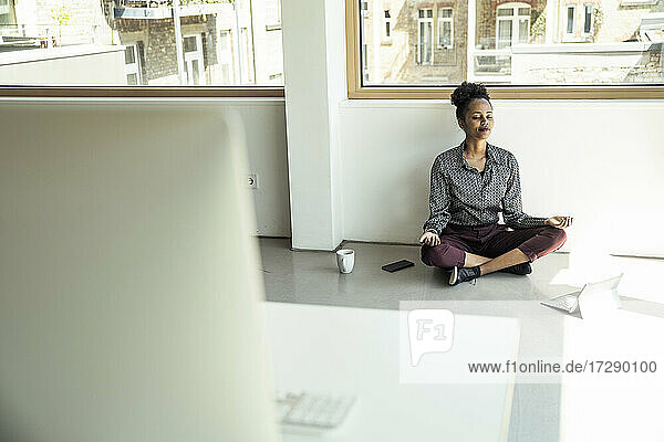 Junge Geschäftsfrau meditiert  während sie im Büro auf dem Boden sitzt