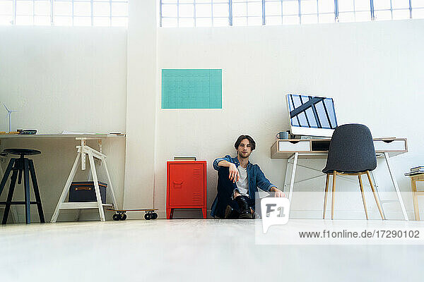 Male entrepreneur sitting on floor by desk in creative office