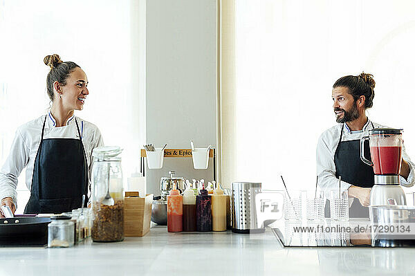 Lächelnde männliche und weibliche Köche arbeiten in der Küche eines Restaurants