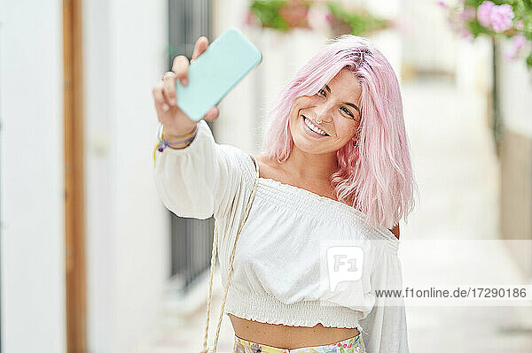 Lächelnde Frau mit rosa Haaren nimmt Selfie durch Smartphone