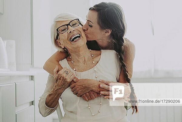 Mid erwachsene Frau mit Arm um küssen Großmutter Wange zu Hause