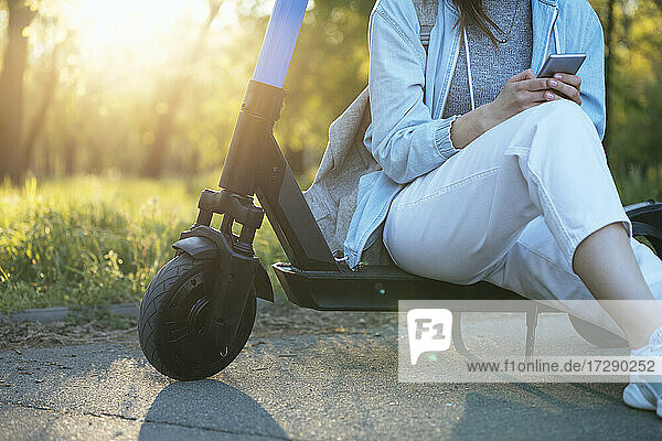 Mittlere erwachsene Frau  die ein Smartphone benutzt  während sie auf einem Elektroroller sitzt