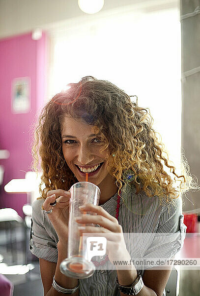 Lockenhaarige Frau trinkt Saft in einem Cafe