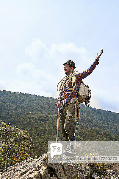 Männlicher Bergsteiger mit erhobener Hand auf einem Berg stehend
