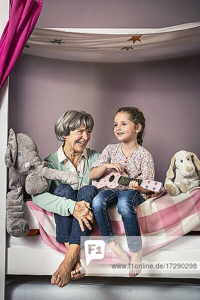 Enkelin spielt Gitarre und sitzt neben der Großmutter auf dem Bett
