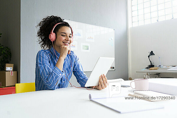 Lächelnde Unternehmerin mit Kopfhörern und digitalem Tablet im Büro