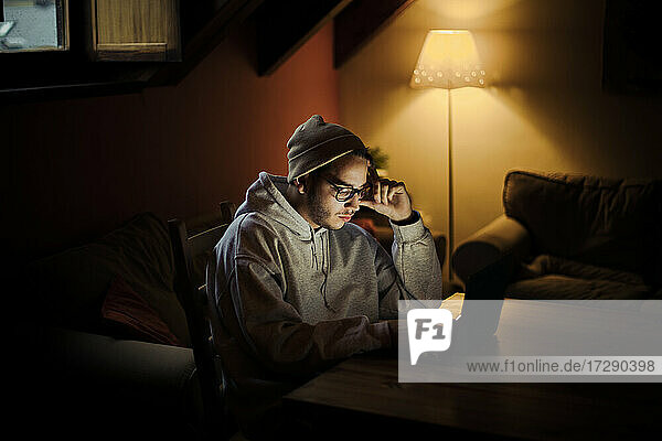 Mann mit Kopf in den Händen benutzt Laptop in Dunkelkammer zu Hause
