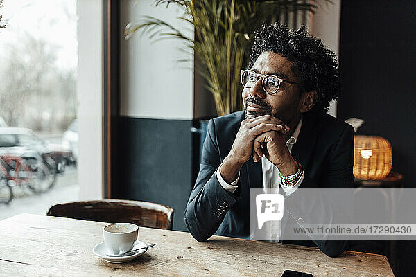 Thoughtful businessman with hand on chin sitting in cafe looking away