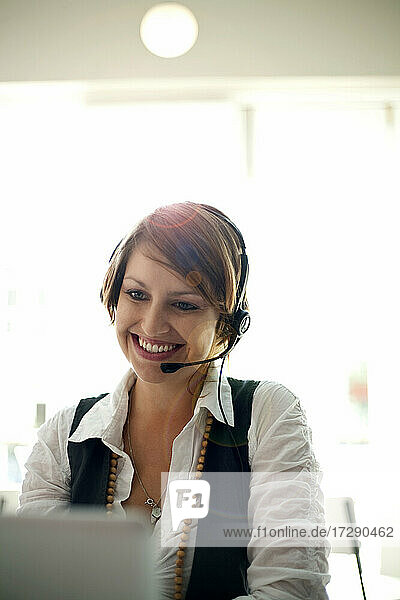 Smiling businesswoman wearing headset during video call on laptop in cafe
