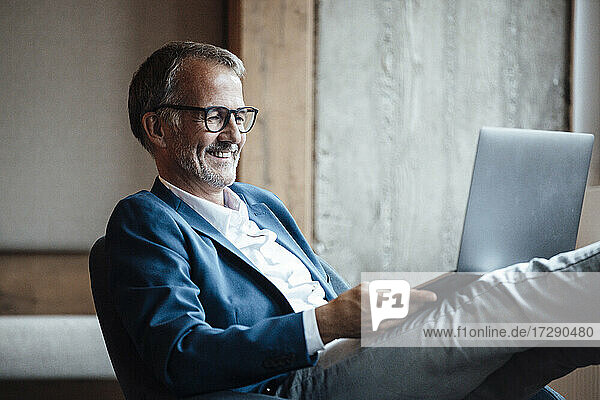 Lächelnder älterer Geschäftsmann arbeitet am Laptop im Büro
