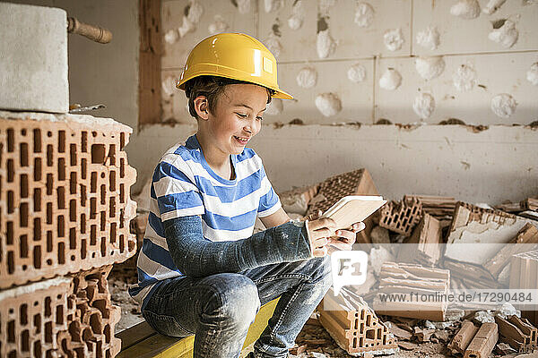 Lächelnder Junge mit Buch  der bei der Renovierung eines Hauses sitzt