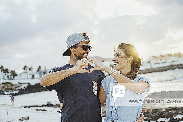 Smiling couple making heart with hands at beach