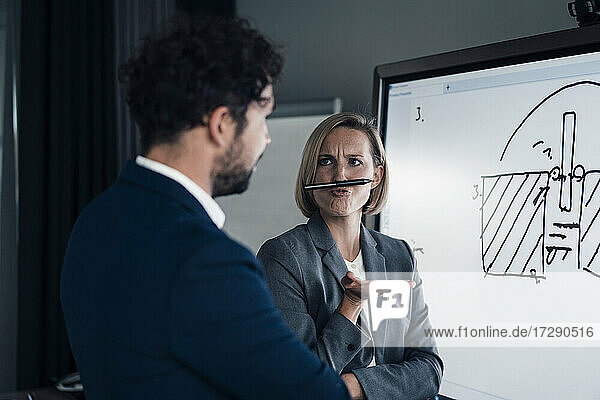 Businesswoman playing with pen while standing by colleague in office