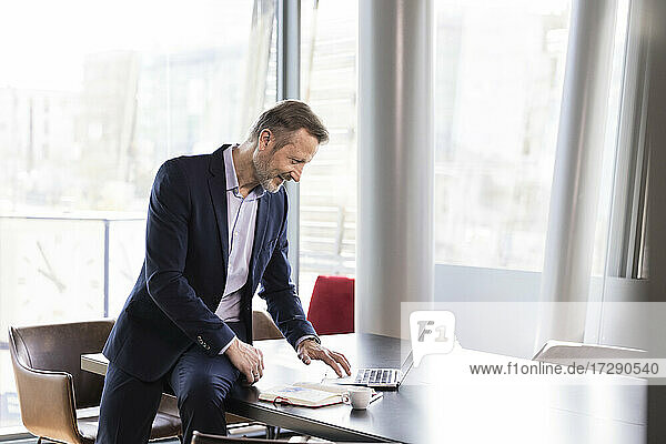 Geschäftsmann  der einen Laptop benutzt  während er auf dem Schreibtisch im Büro sitzt
