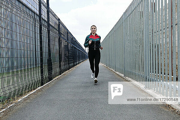 Aktive Sportlerin beim Laufen auf dem Fußweg inmitten von Zäunen