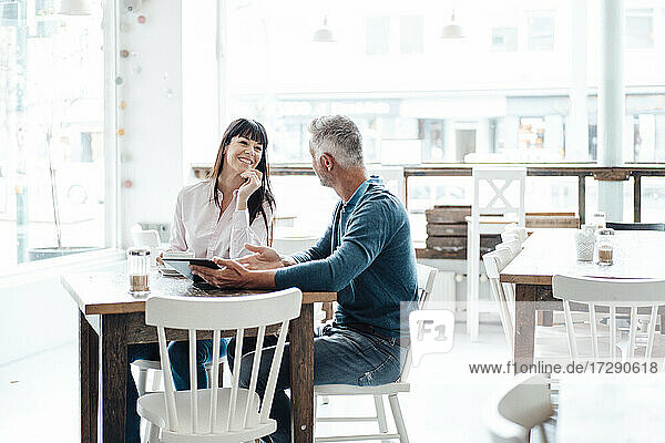 Geschäftsmann mit digitalem Tablet erklärt einem Kollegen  während er in einem Cafe sitzt