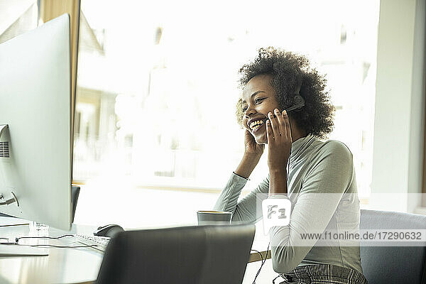 Lächelnde Geschäftsfrau  die ein Headset hält und auf einen Computer im Büro schaut