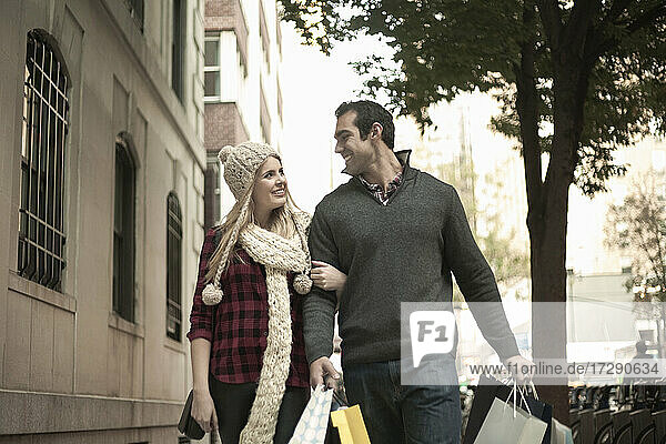 Junger Mann und Frau gehen mit Einkaufstaschen an einem Gebäude vorbei